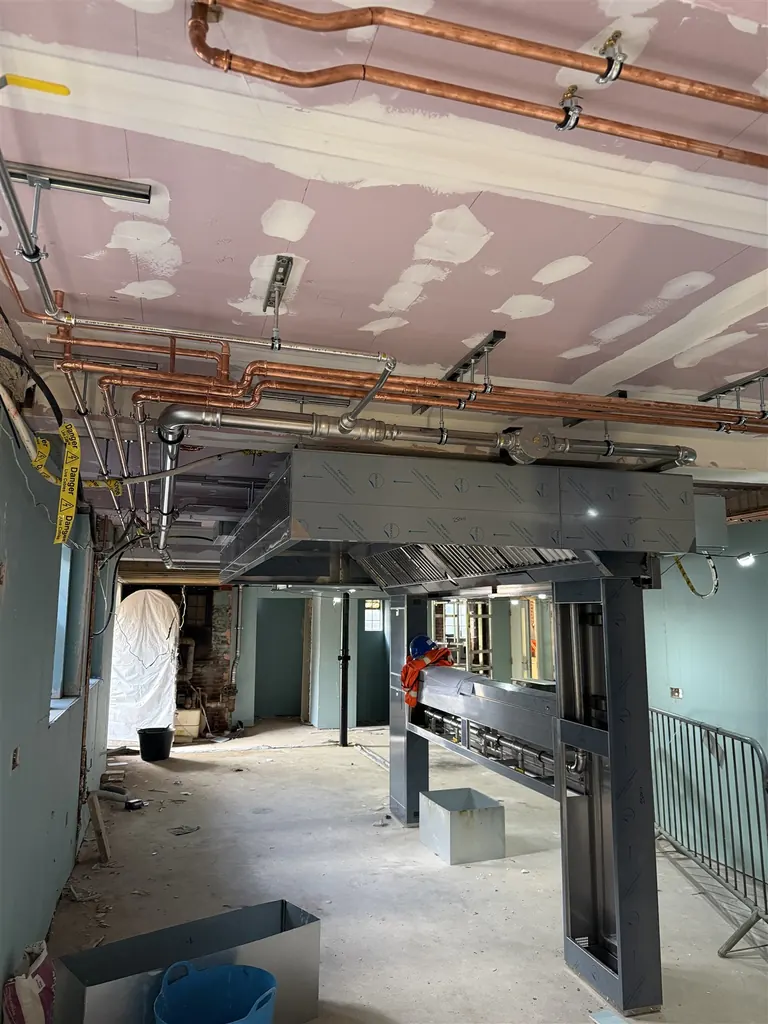 Wide view of stainless-steel gas and copper service pipework above the Beaconsfield Golf Club commercial kitchen during fit-out