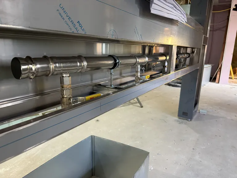 Close view of the stainless-steel kitchen island gas manifold with individual yellow-handled isolation valves
