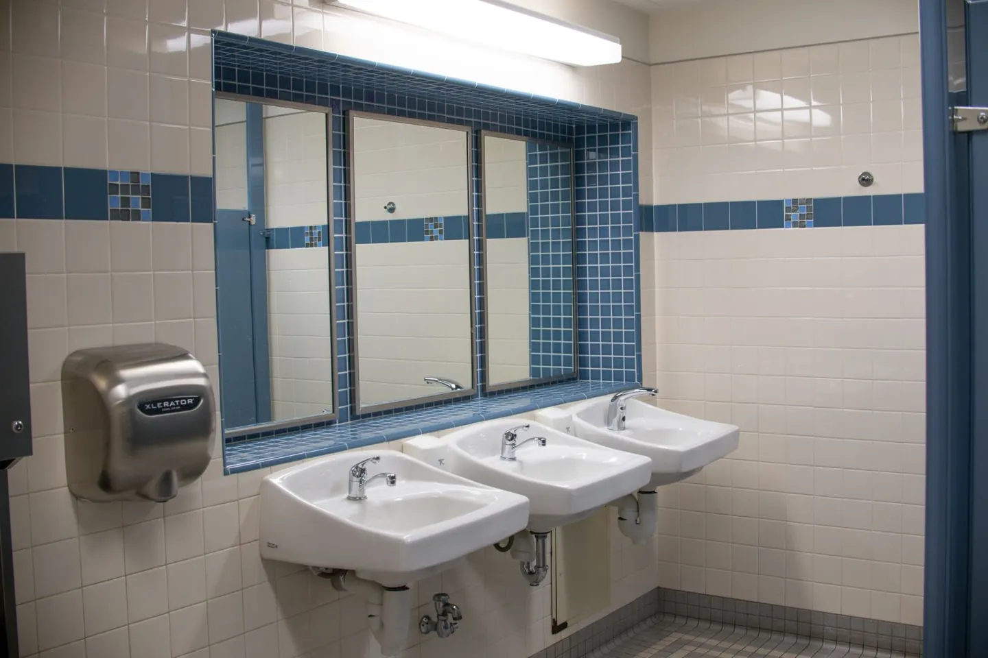 Wall-mounted washbasins, mirrors and a hand dryer in a tiled commercial washroom